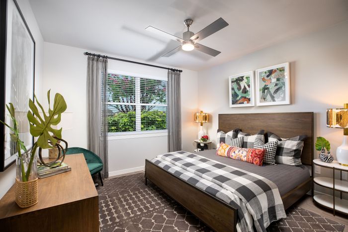 Chic bedroom design with modern ceiling fan, vibrant abstract art, and luxurious bedding in a sunlit space.