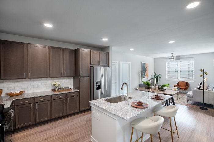 Modern open-concept kitchen and living space with stylish granite countertops, elegant dark wood cabinetry, and warm wood flooring, perfect for entertaining and relaxation.