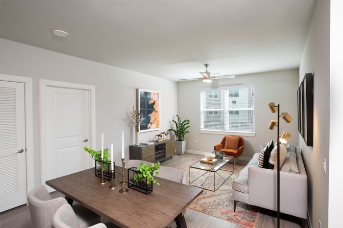 Modern living room with chic decor, featuring a cozy gray sofa, stylish orange chair, elegant wooden dining table, and abundant natural light from large windows.