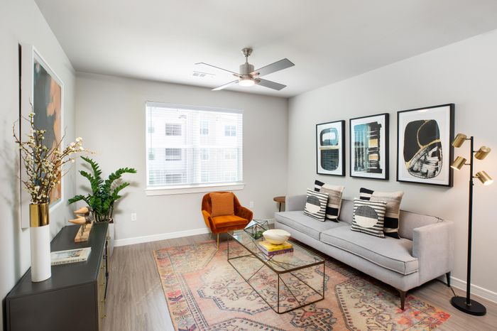 Bright and modern living room with stylish decor, featuring a plush gray sofa, chic art pieces, and a cozy orange chair.