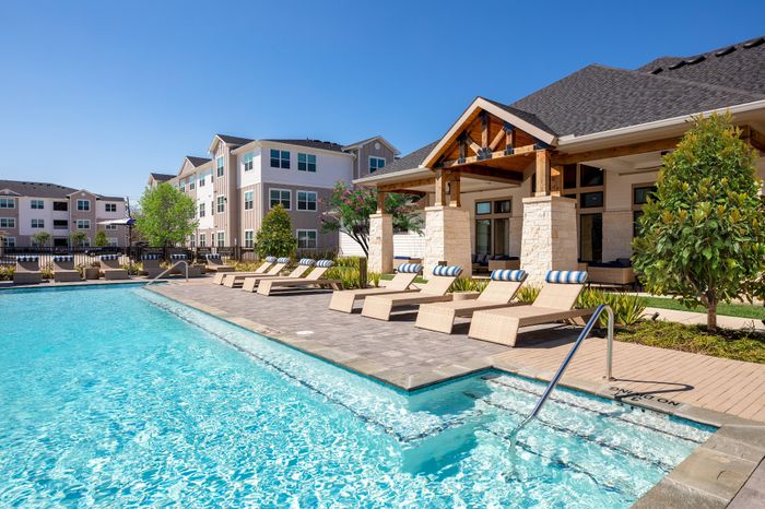 Luxurious apartment complex featuring a sparkling swimming pool, stylish lounge chairs, and modern architecture, perfect for relaxation and leisure.