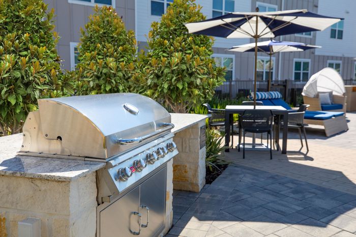Elegant outdoor patio with a modern grill, stylish umbrella-covered dining area, and lush greenery, ideal for relaxing and entertaining guests.