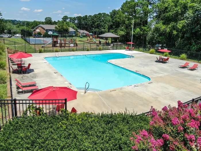 Inviting outdoor pool area with red umbrellas and lounge chairs, perfect for relaxation and enjoying the sun, surrounded by lush greenery.
