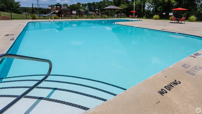 Inviting outdoor swimming pool with crystal clear water, surrounded by a spacious sun deck and vibrant red umbrellas, perfect for relaxation and leisure.