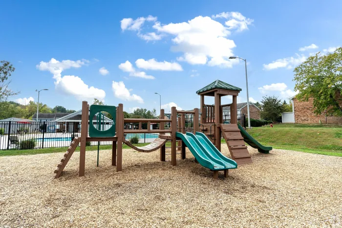 Charming outdoor playground with slides and climbing structures, set against a backdrop of a serene swimming pool and vibrant greenery.