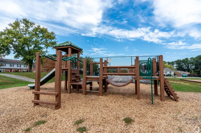 Inviting community playground with a wooden play structure, surrounded by vibrant greenery under a clear blue sky.