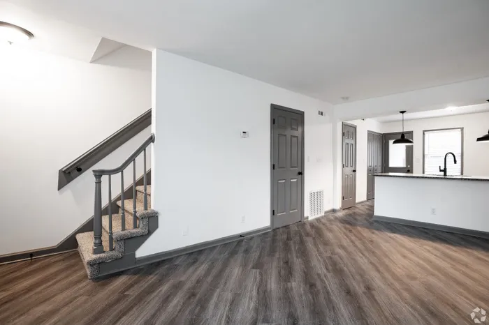 Modern open-concept living space featuring sleek hardwood floors, elegant staircase, and a bright kitchen with stylish pendant lighting.