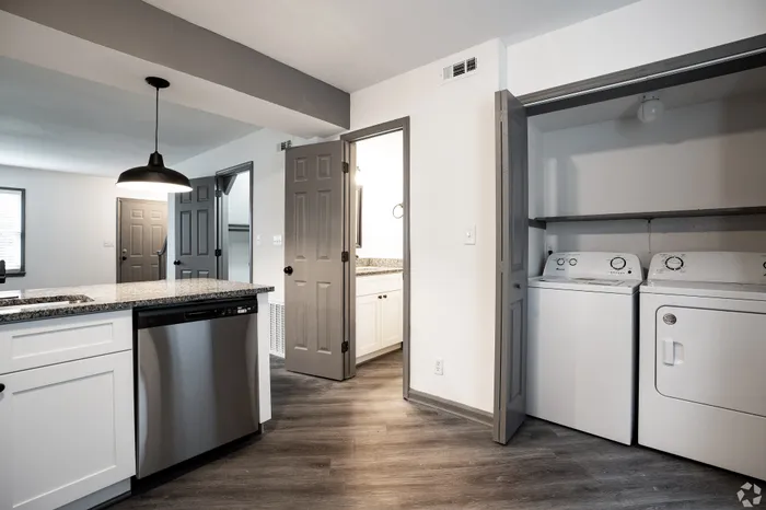 Modern apartment interior featuring a sleek kitchen with granite countertops and stainless steel appliances, adjacent to a convenient laundry area with washer and dryer.