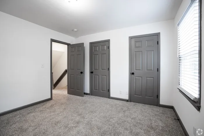 Bright, airy room with three stylish gray doors and plush carpeting, perfect for a cozy retreat.