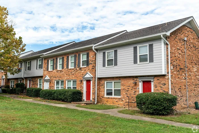 Charming townhouse row with brick facade, vibrant red doors, and lush greenery in a serene neighborhood setting.
