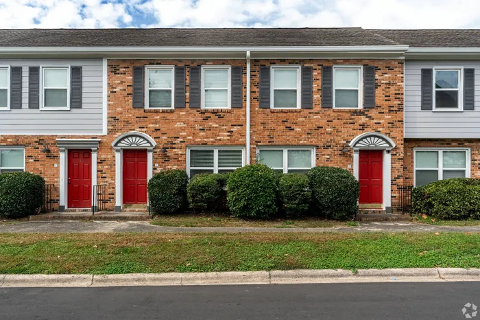 Charming brick townhouse with vibrant red doors and lush greenery, offering a welcoming and stylish facade.