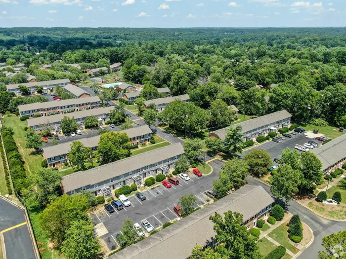 Charming aerial view of a cozy apartment complex surrounded by lush greenery and spacious parking, offering a serene living experience.