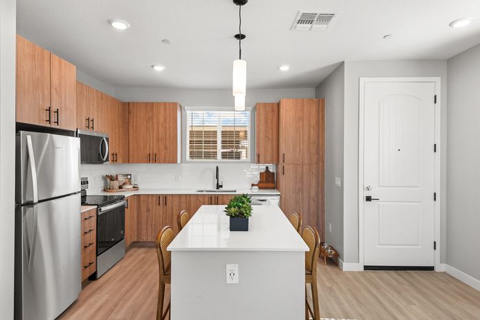 Modern kitchen with sleek stainless steel appliances, elegant wooden cabinetry, and a stylish island with seating, illuminated by soft pendant lighting.