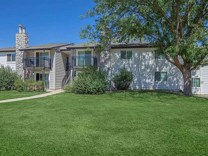 Charming apartment exterior with balconies, lush green lawn, and mature tree, providing a serene and inviting atmosphere.