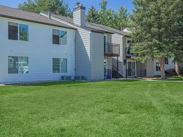 Charming apartment exterior featuring modern balconies, lush green lawn, and beautiful trees.