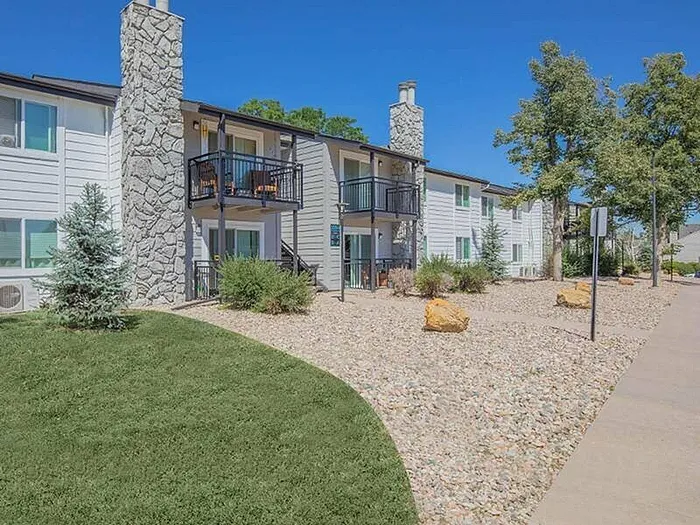 Charming apartment complex with modern balconies, stone accents, and a beautifully landscaped yard under a clear blue sky.