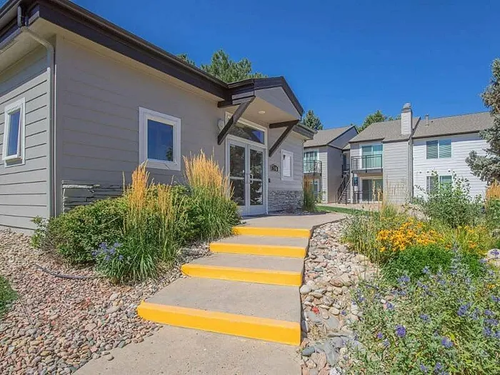 Charming modern apartment exterior with vibrant landscaping and inviting entrance steps, bathed in sunlight.