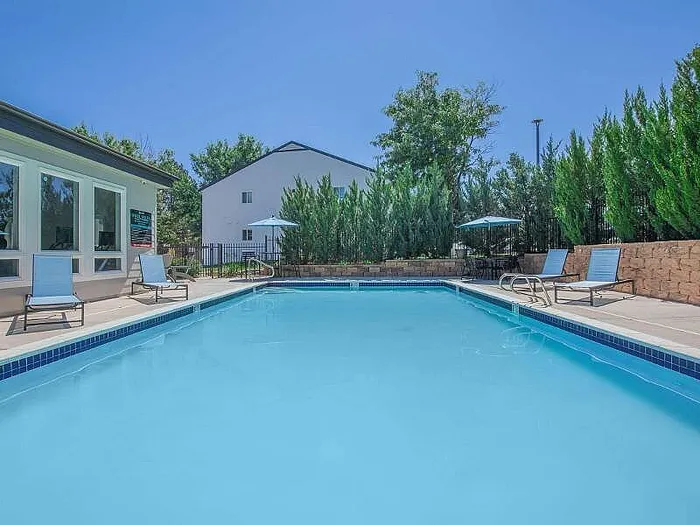 Inviting outdoor pool area with sun loungers and umbrellas, surrounded by lush greenery, perfect for relaxation.