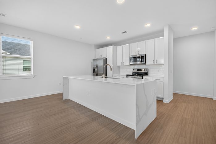 Modern kitchen with sleek white cabinetry, stainless steel appliances, and a stylish island, complemented by elegant wood flooring.