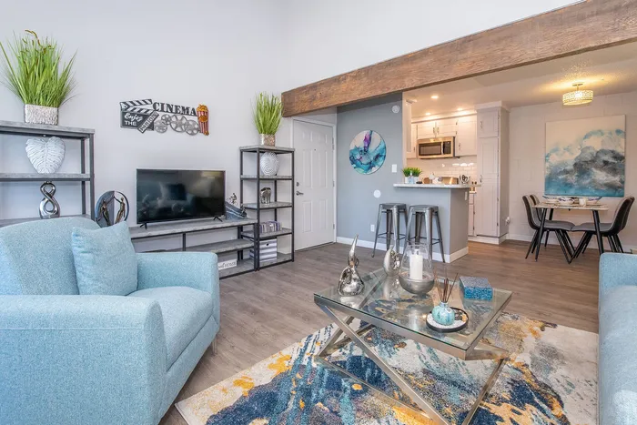 Contemporary living room with elegant decor, featuring a cozy blue armchair, stylish glass coffee table, and modern kitchen with dining area.