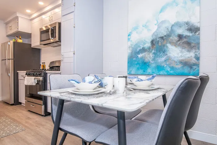 Chic modern kitchen with stainless steel appliances, elegant marble dining table set for four, and vibrant blue abstract art.