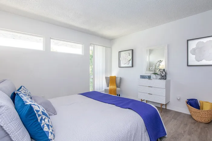 Bright and inviting modern bedroom with blue and gray accents, featuring a cozy bed, stylish dresser, and vivid natural light.