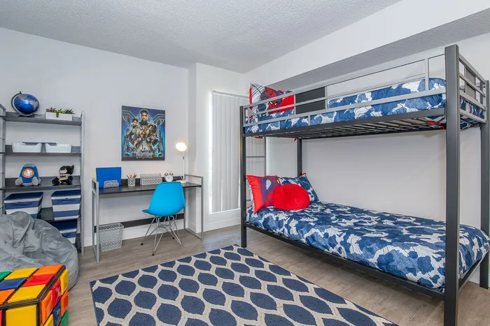Vibrant children's bedroom featuring stylish bunk beds, a cozy study area with a sleek desk and blue chair, and playful decor accents for a lively atmosphere.