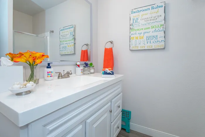 Chic and inviting bathroom with modern decor, featuring a sleek white vanity, vibrant orange flowers, and a playful decor sign for an uplifting ambiance.