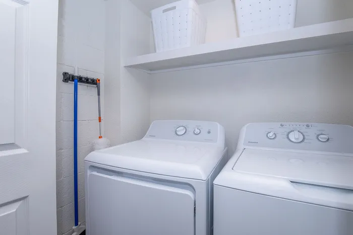 Modern laundry room featuring sleek washer and dryer with white shelving and storage baskets above.