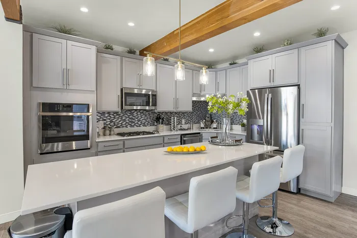 Sleek modern kitchen with gray cabinets, stainless steel appliances, stylish backsplash, and elegant pendant lighting over a spacious island with seating.