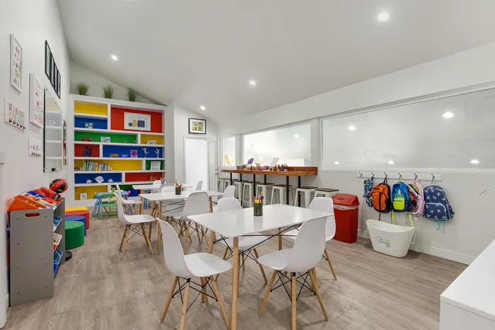 Bright and inviting children's playroom with colorful bookcases, white tables, and playful decor.