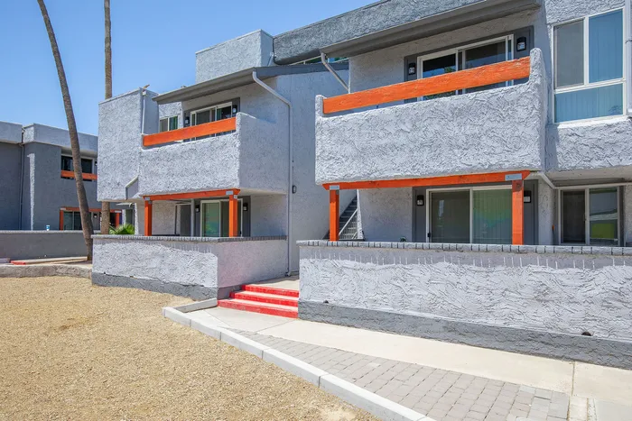 Modern apartment exterior with sleek gray stucco, vibrant orange accents, and inviting balconies offering a stylish urban living experience.