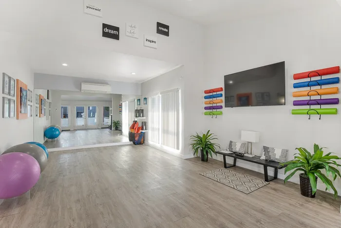 Modern fitness and yoga studio with elegant wood floors, vibrant yoga mats, relaxing seating area, and motivational wall art.