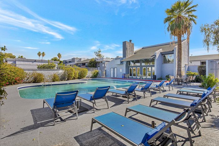 Charming apartment complex with inviting pool, surrounded by lush greenery and stylish blue loungers, perfect for relaxation.