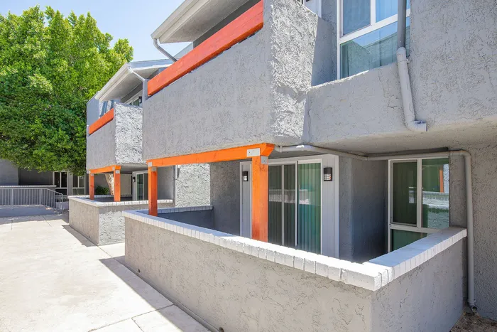 Charming apartment exterior featuring modern architecture with vibrant orange accents, ample natural light through large windows, and spacious balconies amidst lush greenery.