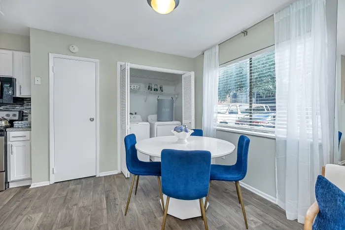 Chic dining area featuring a round white table, vibrant blue chairs, and natural light streaming through floor-to-ceiling windows.