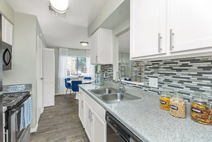 Chic modern kitchen with sleek cabinetry, granite countertops, and elegant mosaic backsplash leading to a bright dining area with stylish blue chairs.