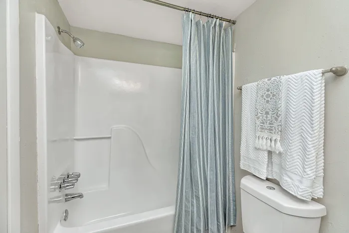 Bright and modern bathroom featuring an inviting white bathtub with elegant chrome fixtures, complemented by a stylish striped shower curtain and neatly arranged textured towels.