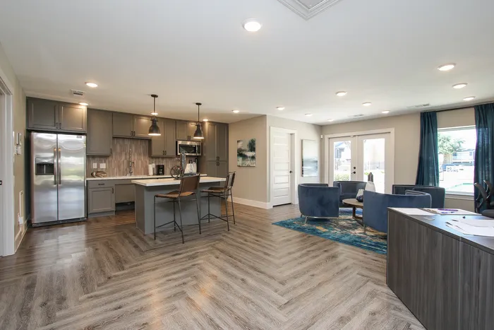 Contemporary open-concept kitchen and living area featuring sleek gray cabinets, a modern island with bar seating, and elegant wood flooring, ideal for stylish entertaining.