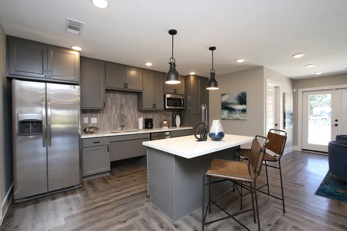 Modern kitchen with sleek gray cabinetry, stainless steel appliances, and stylish pendant lighting over a chic breakfast bar with leather stools.