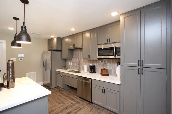 Modern kitchen with elegant gray cabinets, stainless steel appliances, and sleek pendant lighting.