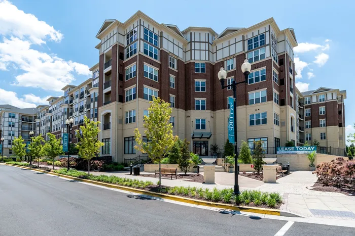 Modern multi-story apartment building with elegant architecture, lush landscaping, and a welcoming entrance featuring clear skies above.