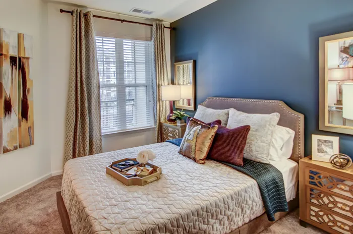 Cozy bedroom with elegant decor, featuring a plush bed, stylish accent pillows, and a chic nightstand against a rich blue accent wall.