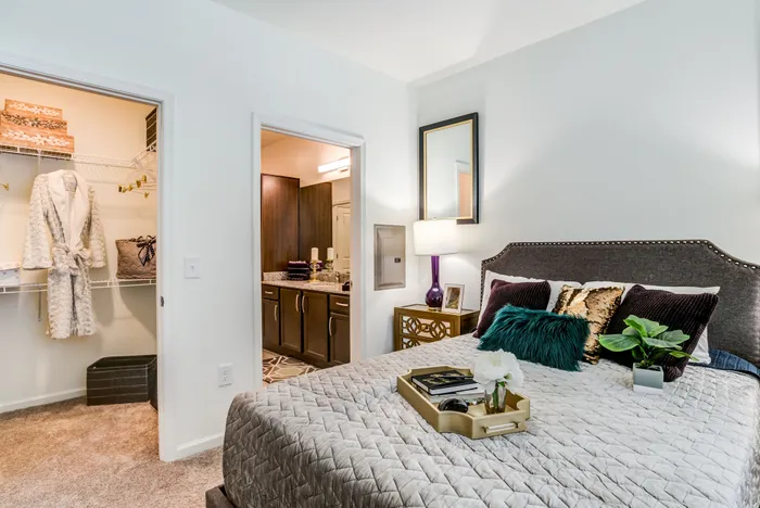 Chic bedroom with elegant decor, featuring a plush bed, stylish bedside lamp, and a walk-in closet. Luxurious ensuite bathroom visible beyond the door.