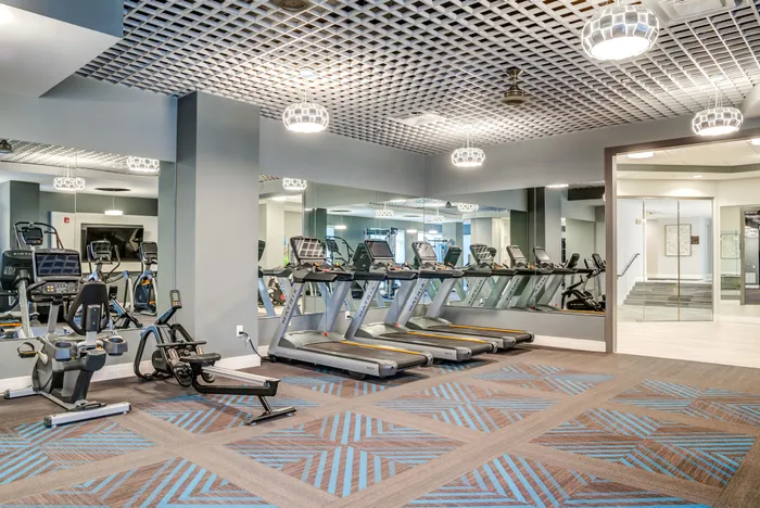 Modern fitness center with state-of-the-art treadmills, recumbent bikes, and rowing machine, reflecting in large mirrors for an open feel.
