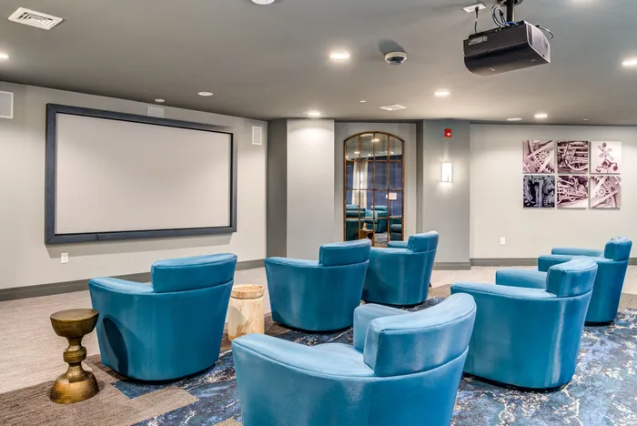 Modern apartment theater room featuring plush blue seating, large projector screen, and stylish decor for an immersive entertainment experience.