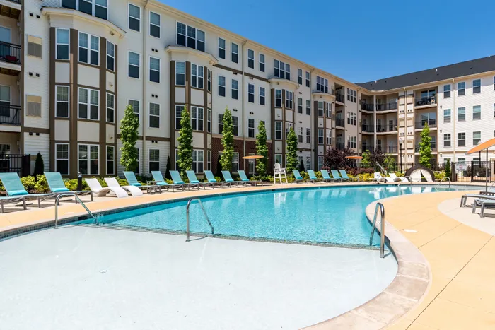 Luxurious apartment complex showcasing a stunning outdoor pool area with sleek lounge chairs and lush landscaping, perfect for relaxation.
