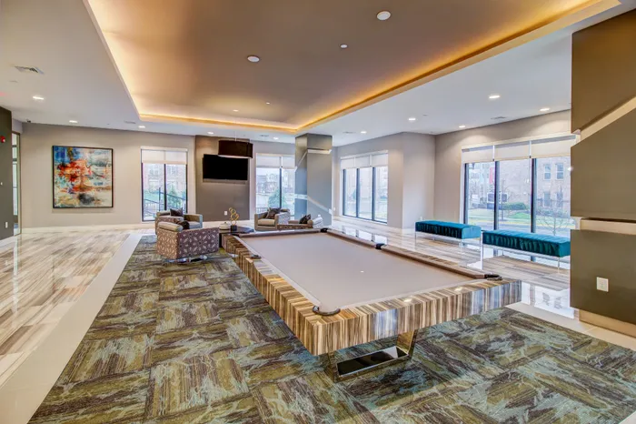 Luxurious apartment recreation area with a stylish billiards table, modern seating, and expansive windows providing ample natural light.