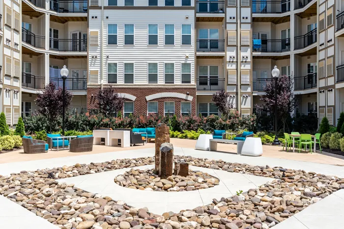 Modern apartment complex with stylish balconies, vibrant outdoor seating, and a chic stone fountain centerpiece.