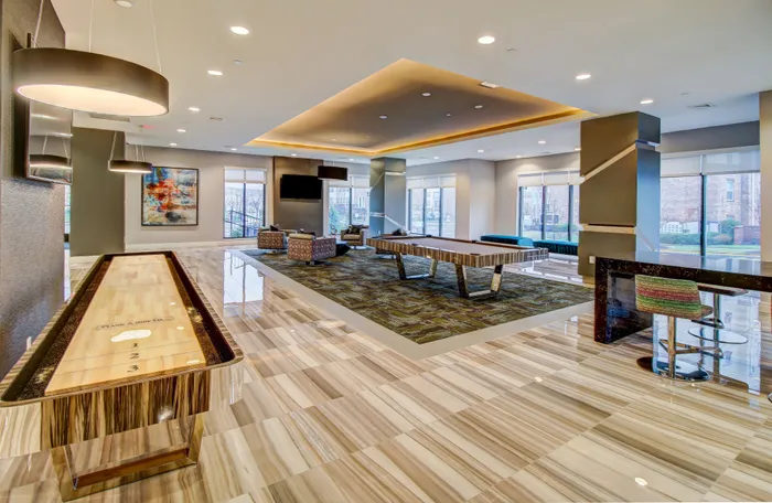 Luxurious game room with polished flooring, featuring a shuffleboard table, pool table, modern seating, and vibrant artwork for entertainment and relaxation.